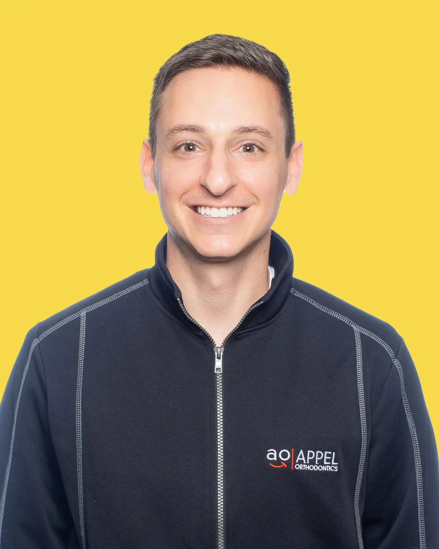 Smiling man in Appel Orthodontics jacket, yellow background